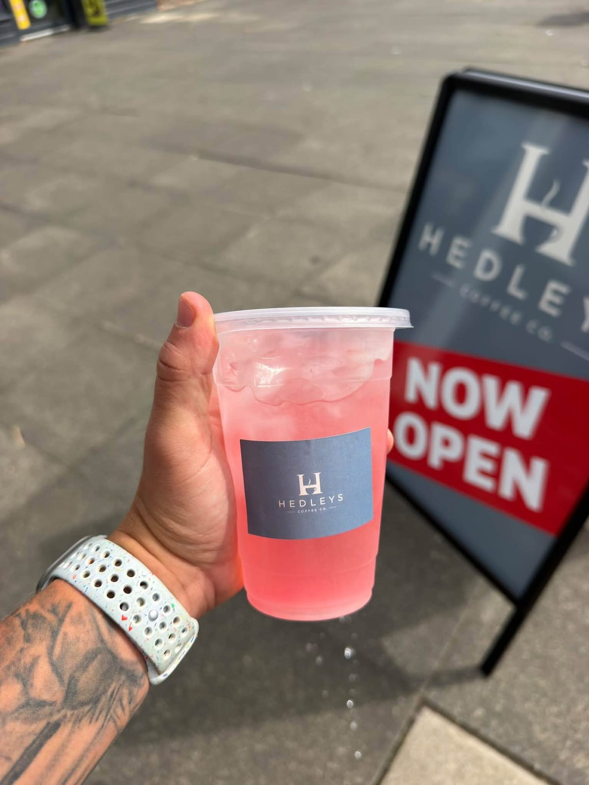 A strawberry lemonade held up in front of the Hedleys Now Open sign